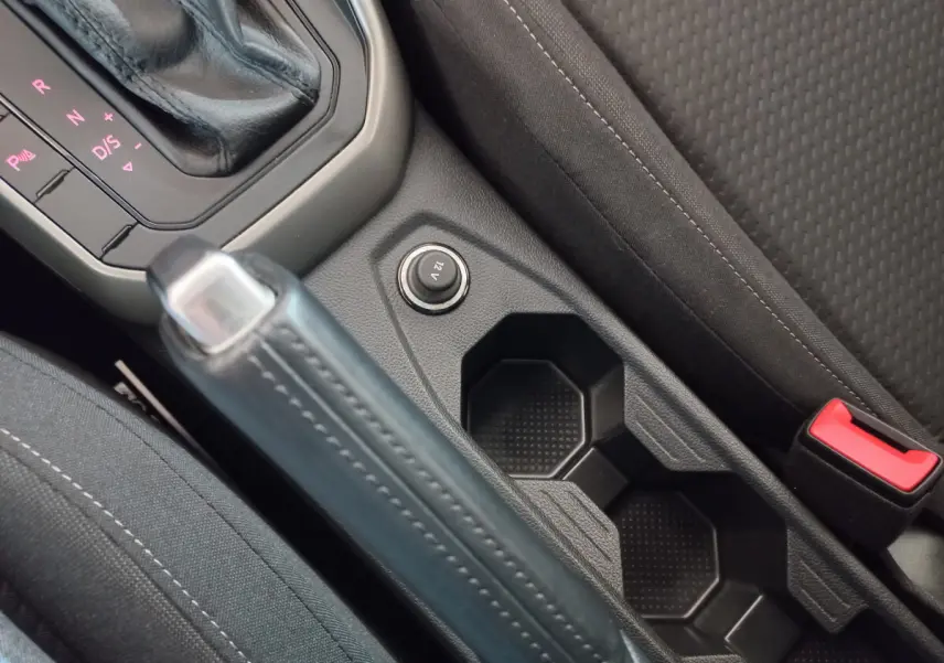 Gros plan sur la console centrale noire de la Volkswagen Polo 2020, avec frein à main, prise 12V et porte-gobelets.