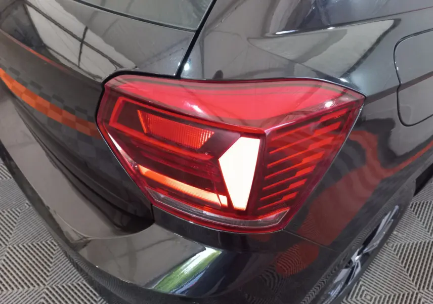 Gros plan sur le feu arrière droit rouge d'une Volkswagen Polo noire, avec une partie de la carrosserie visible.