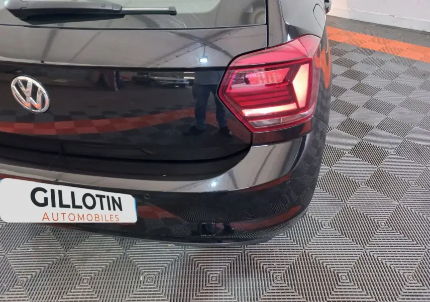 Vue rapprochée de l'arrière droit d'une Volkswagen Polo noire avec feu arrière allumé et logo VW visible.