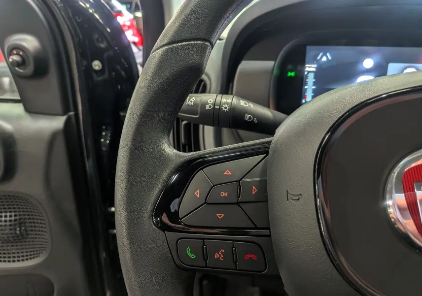 Gros plan sur le volant noir de la Fiat Panda 2025 hybride avec commandes intégrées et tableau de bord numérique partiel.