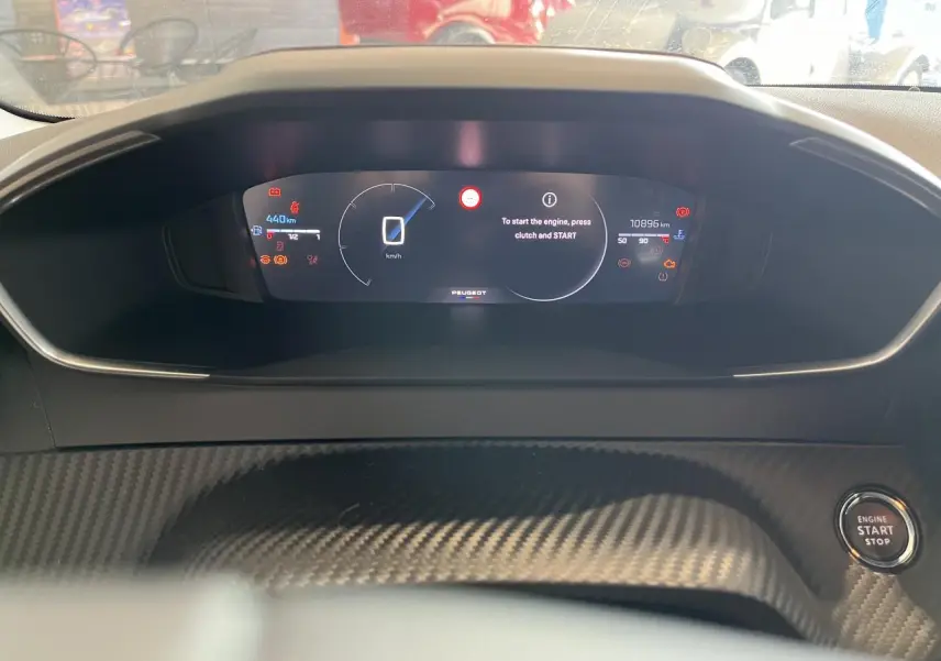 Vue rapprochée du combiné numérique Peugeot 208 2024 avec affichage digital et bouton start/stop sur console carbone.