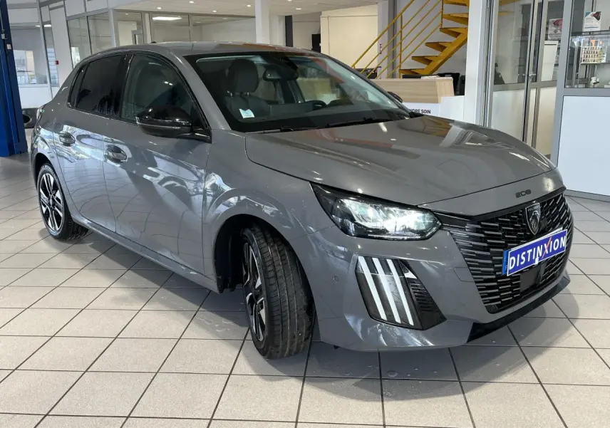 Peugeot 208 gris clair sélénium vue 3/4 avant droit avec calandre noire et feux LED 3 griffes allumés.