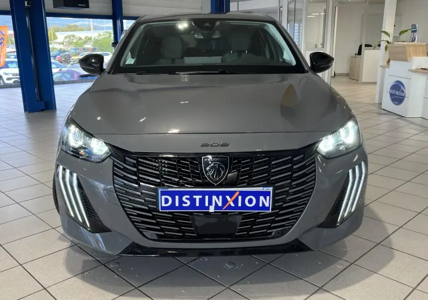Vue avant d'une Peugeot 208 2024 gris clair Selenium avec calandre noire et feux LED allumés en showroom.