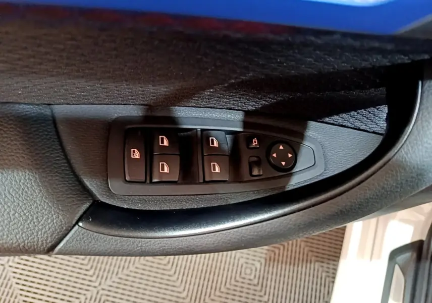 Gros plan sur les commandes des vitres électriques et rétroviseurs côté gauche d'une BMW X1 blanc 2022.