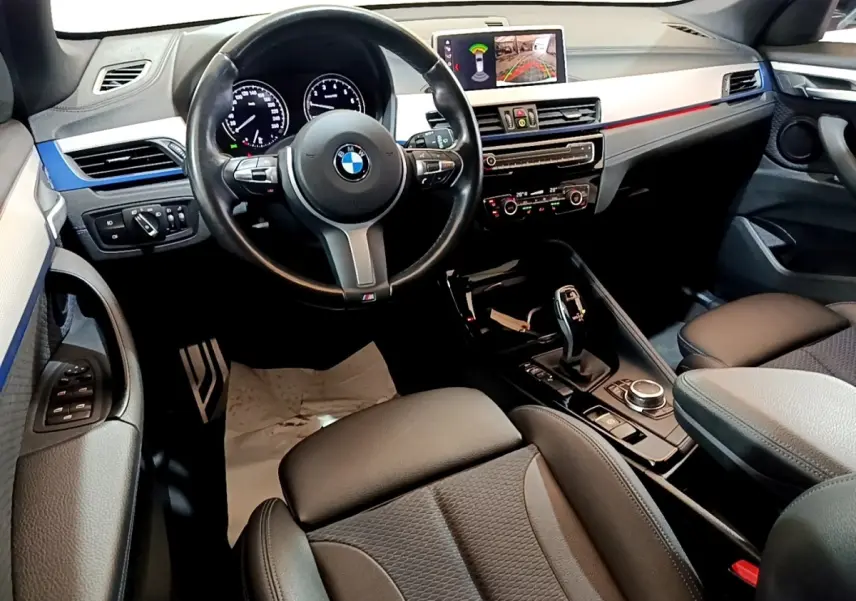 Vue intérieure avant droite du BMW X1 sDrive18i M Sport 2022, volant cuir, écran tactile et console centrale noire.