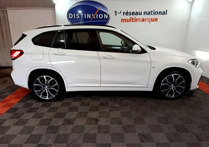 BMW X1 sDrive18i M Sport blanc vue de profil côté gauche, avec jantes alliage et feux arrière allumés.