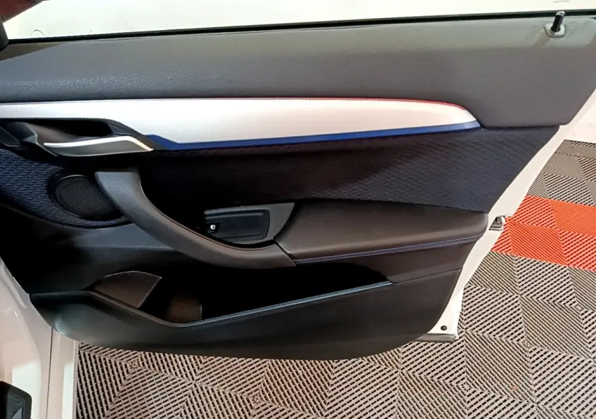 Vue rapprochée de la porte avant droite blanche du BMW X1 sDrive18i M Sport avec garniture noire et insert argenté.