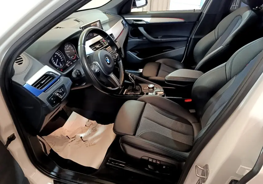 Vue intérieure côté conducteur de la BMW X1 blanc, montrant sièges noirs et tableau de bord avec écran tactile.