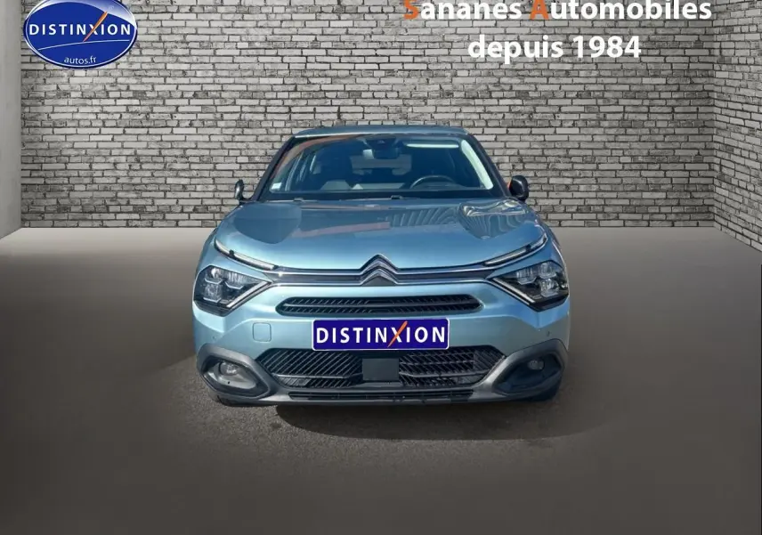 Vue de face d'une Citroën C4 bleu clair 2021 avec calandre distinctive et phares modernes, sur fond de mur en briques.