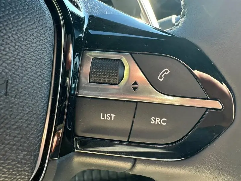 Gros plan sur les commandes au volant noir du Peugeot 2008 1.2 Hybrid 145ch Allure 2025, boutons LIST, SRC et téléphone.