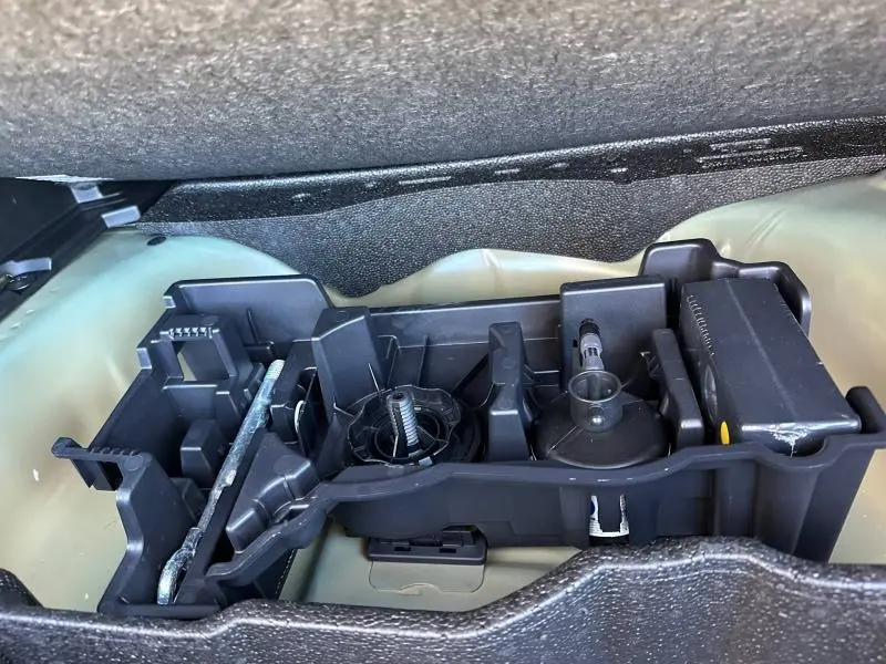 Gros plan sur le rangement d'outils en plastique noir dans le coffre d'un Peugeot 2008 bleu hybride 2025.