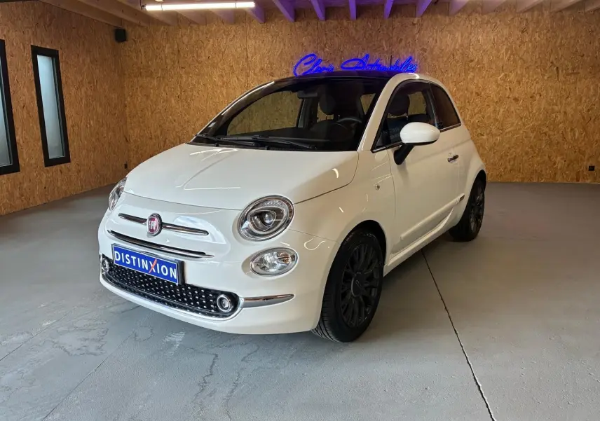 Fiat 500 blanc crème vue 3/4 avant droit dans un intérieur avec mur en bois et jantes noires.