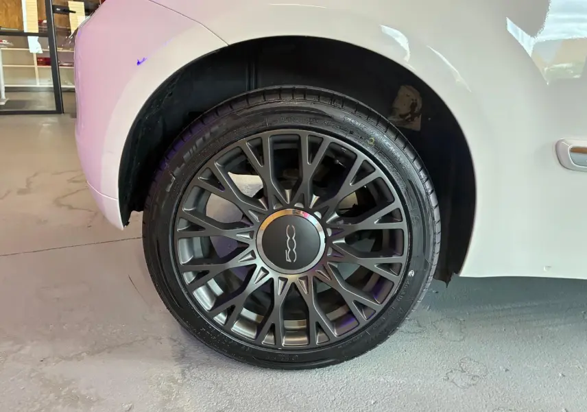 Gros plan sur la roue arrière droite d'une FIAT 500 blanc crème, mettant en valeur la jante noire à multiples branches.