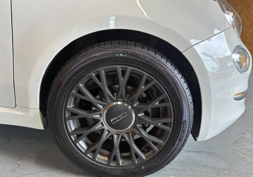 Gros plan sur la roue avant droite d'une FIAT 500 blanc crème, mettant en valeur la jante foncée au design ajouré.