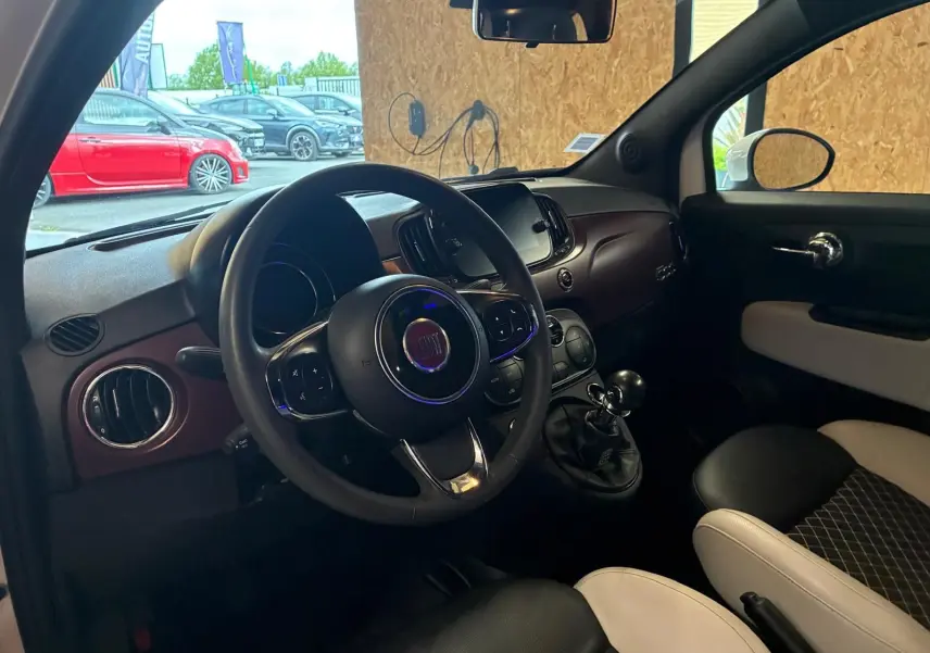 Intérieur de la Fiat 500 blanc crème vu côté conducteur, volant multifonction et levier de vitesse manuel visibles.