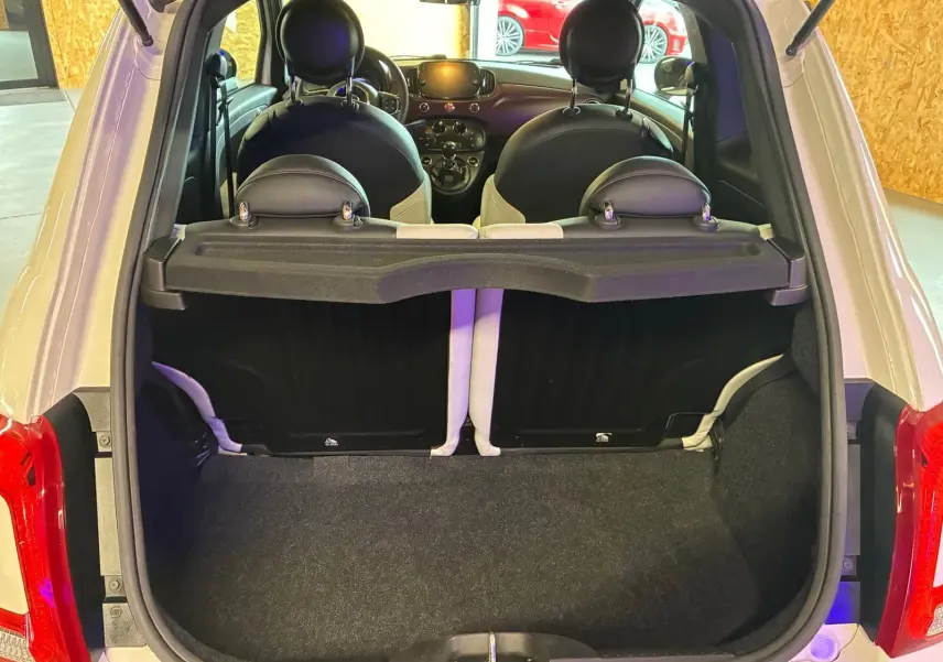 Vue arrière ouverte du coffre d'une FIAT 500 blanc crème, avec intérieur noir et blanc visible jusqu'au tableau de bord.