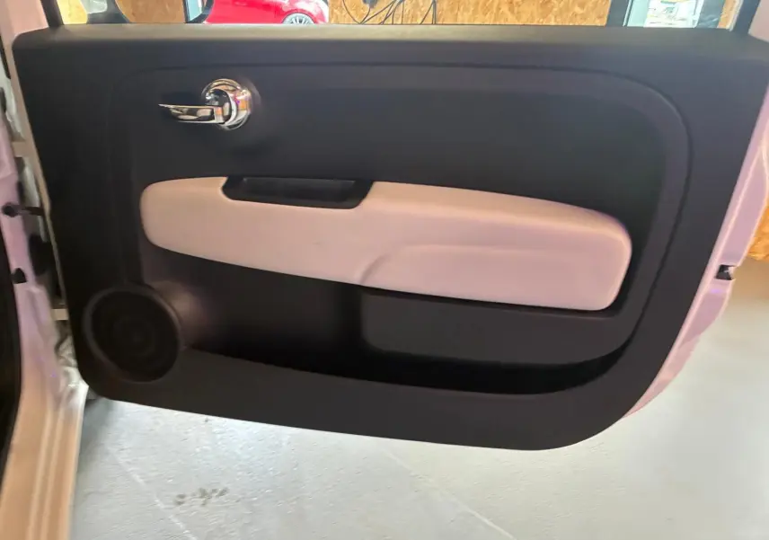 Vue intérieure de la porte avant gauche de la Fiat 500 blanche crème, avec poignée chrome et accoudoir clair.