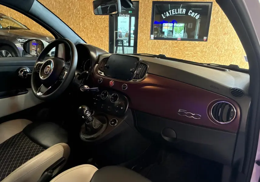 Vue intérieure côté conducteur de la Fiat 500 blanche crème, tableau de bord bordeaux avec logo 500 et volant noir.