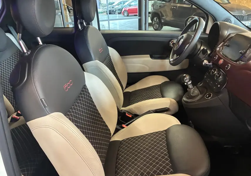 Vue intérieure côté conducteur de la Fiat 500 blanc crème, sièges noir et crème avec logo 500 brodé rouge.