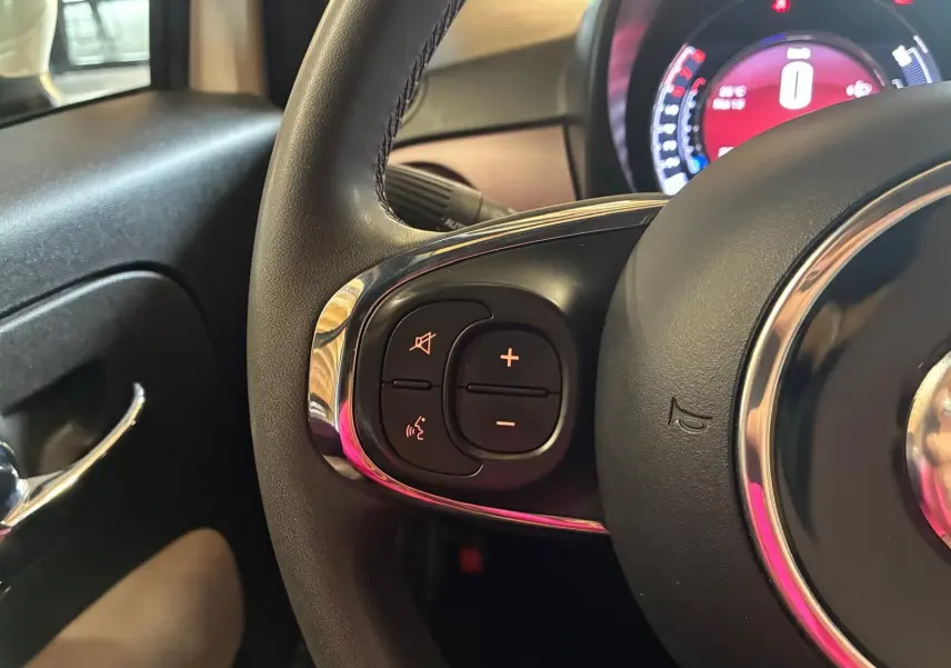 Gros plan sur le volant côté gauche d’une Fiat 500 blanc crème, montrant les commandes audio intégrées.
