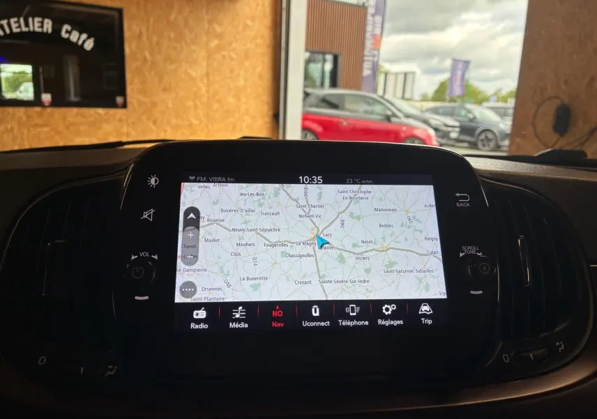 Vue intérieure du tableau de bord de la Fiat 500 blanc crème, mettant en valeur l'écran tactile de navigation allumé.