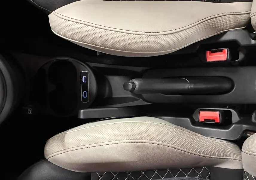 Vue plongeante sur la console centrale du Fiat 500 blanc crème, montrant frein à main et sièges en cuir bicolore noir et crème.