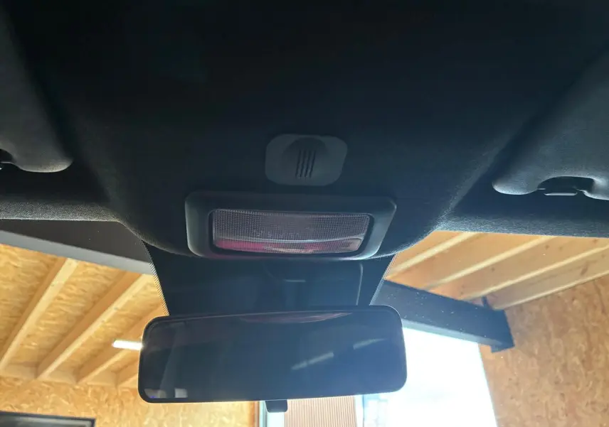 Vue intérieure centrée sur le rétroviseur intérieur et la lumière de plafond d'une Fiat 500 blanc crème.