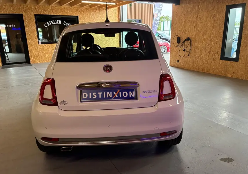 Vue arrière d'une FIAT 500 blanc crème hybride, stationnée en intérieur avec plaque Distinxion visible.