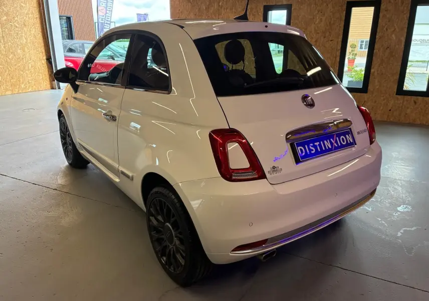 Vue 3/4 arrière droite d'une FIAT 500 blanc crème 2021 avec jantes noires et intérieur visible à travers les vitres.