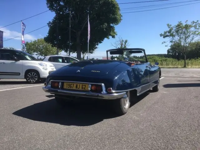 Vue 3/4 arrière d'une Citroën DS3 Cabriolet Chapron bleu marine de 1967 avec capote ouverte sur parking.