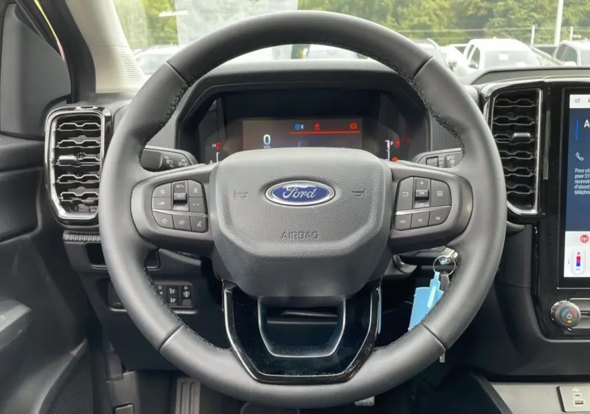 Vue rapprochée du volant noir du Ford Ranger 2025 avec commandes intégrées et tableau de bord numérique.