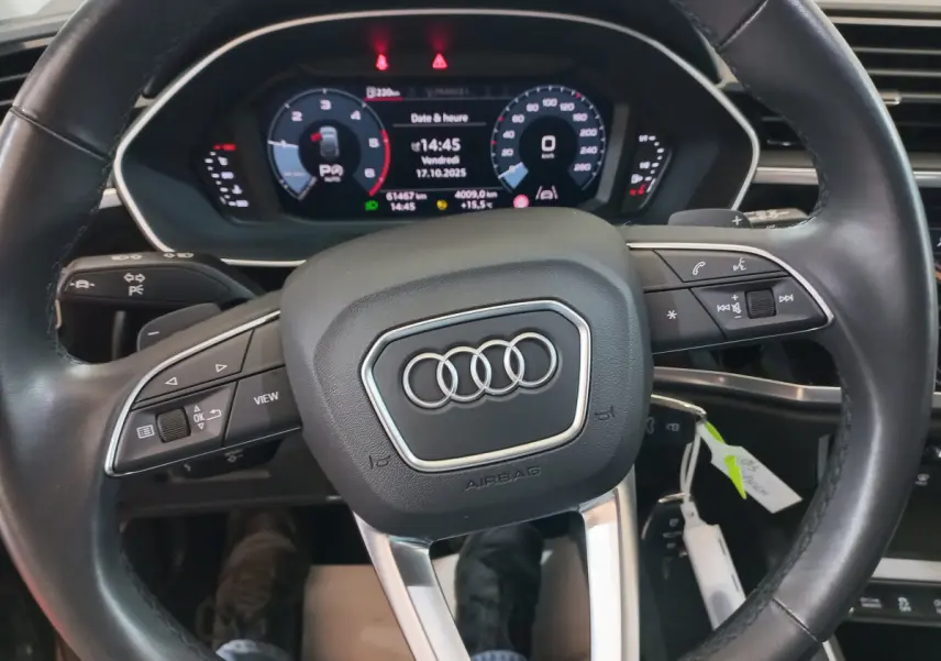 Vue rapprochée du volant cuir noir d'un Audi Q3 Sportback 35 TDI 150 S tronic avec tableau de bord numérique allumé.