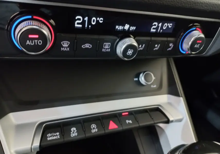 Gros plan sur la console centrale de l'Audi Q3 Sportback noire, affichant la climatisation digitale à 21°C.