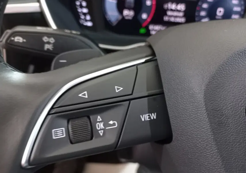 Gros plan sur les commandes gauche du volant cuir d'un Audi Q3 Sportback noir, avec affichage numérique en arrière-plan.