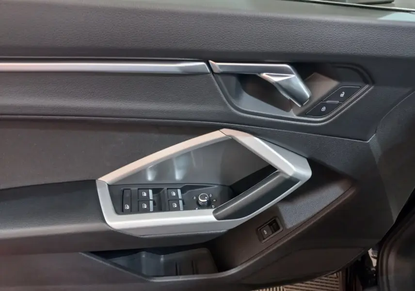 Gros plan sur la porte côté conducteur de l'Audi Q3 Sportback noire, montrant les commandes des vitres et la poignée argentée.