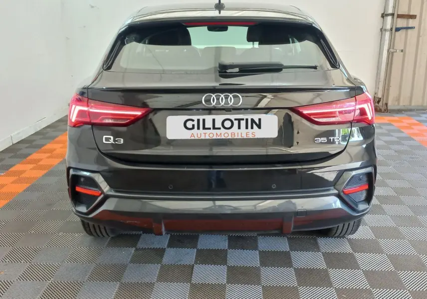 Vue arrière d'un Audi Q3 Sportback noir 35 TDI avec feux LED et logo distinctif sur fond intérieur showroom.
