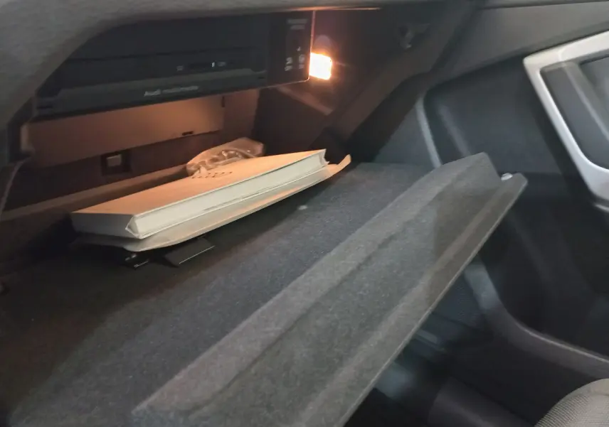 Gros plan sur la boîte à gants ouverte de l'Audi Q3 Sportback 35 TDI noir, avec manuel et éclairage intérieur allumé.