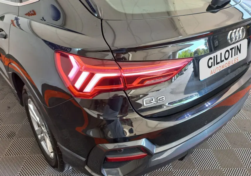 Vue 3/4 arrière droite d'un Audi Q3 Sportback noir avec feux arrière LED allumés et logo Q3 visible.