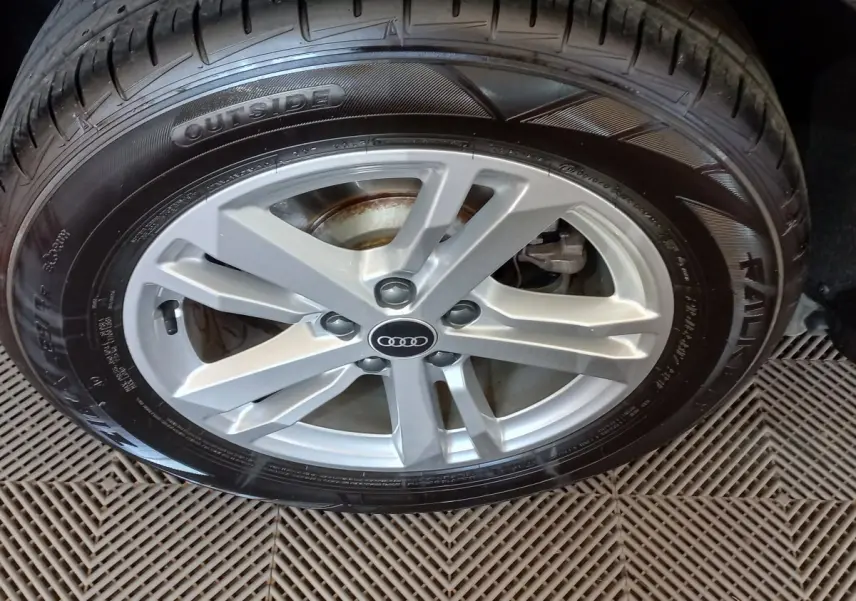 Gros plan sur la jante argentée avec logo Audi d’un Q3 Sportback noir, mettant en valeur le pneu et la roue avant droite.