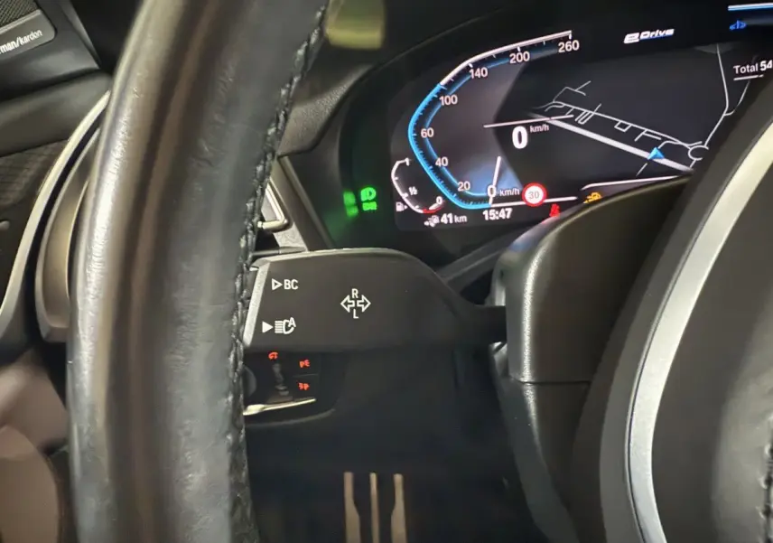 Gros plan sur le tableau de bord numérique et le volant cuir noir de la BMW X3 xDrive30e 2023, affichage vitesse et navigation.