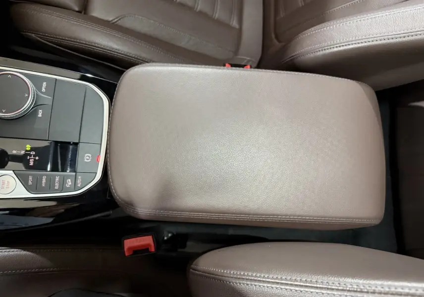 Vue rapprochée de l'accoudoir central en cuir marron et de la console centrale avec commandes du BMW X3 xDrive30e bleu 2023.