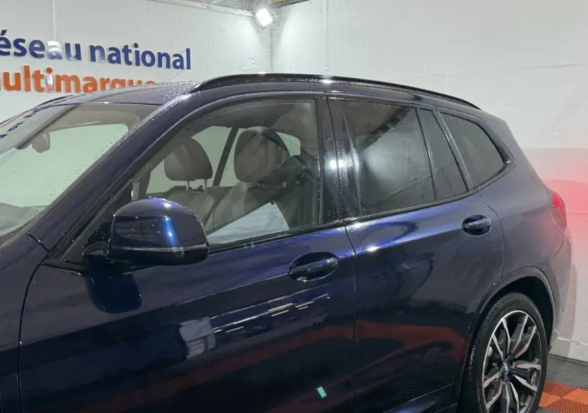 Vue latérale gauche d'un BMW X3 xDrive30e bleu avec jantes alliage et vitres teintées dans un garage.