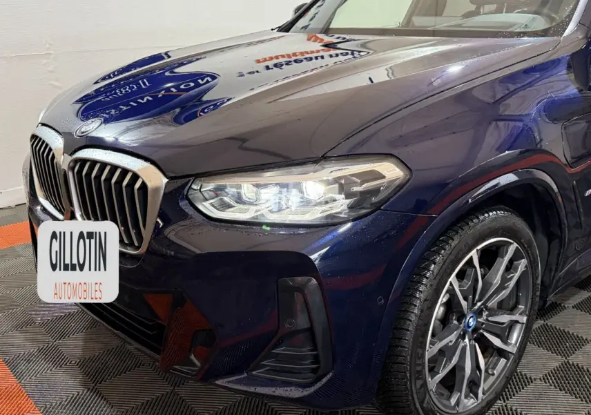 Vue 3/4 avant droit d’un BMW X3 xDrive30e bleu avec phares LED allumés et jantes alliage distinctives.