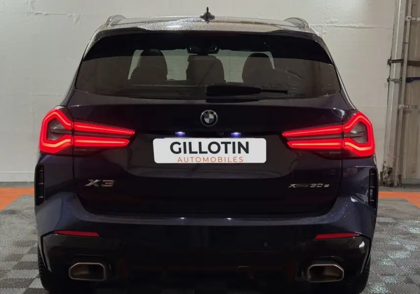 Vue arrière d’un BMW X3 xDrive30e bleu 2023 avec feux LED allumés et double sortie d’échappement rectangulaire.