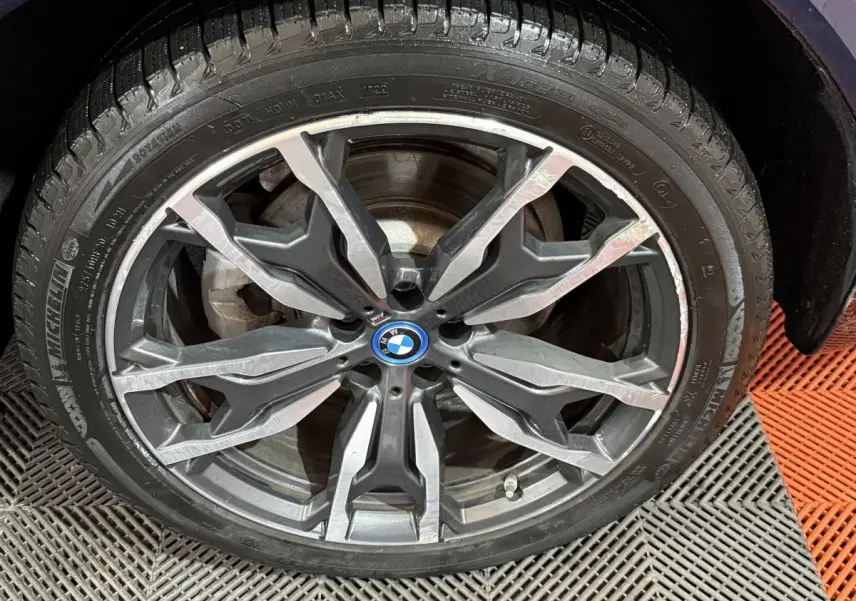 Gros plan sur la jante alliage noire et argentée du BMW X3 xDrive30e bleu, avec logo BMW central visible.