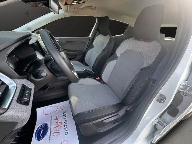 Vue intérieure côté conducteur de la Renault Clio V blanche, avec sellerie textile gris à motif 3D et volant textile grainé.