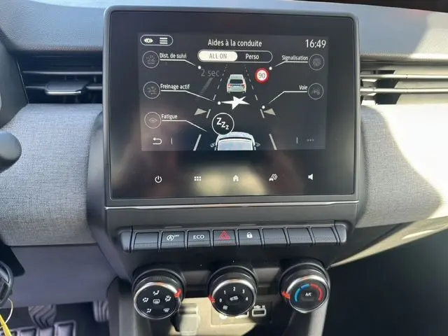 Vue rapprochée de la console centrale de la Renault Clio V blanche, affichant l'écran tactile des aides à la conduite.