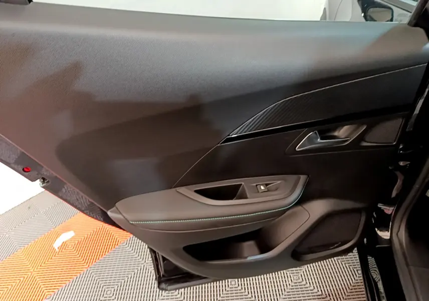 Vue rapprochée de la porte arrière droite noire du Peugeot 2008 PureTech 130 avec garniture carbone et surpiqûres bleues.