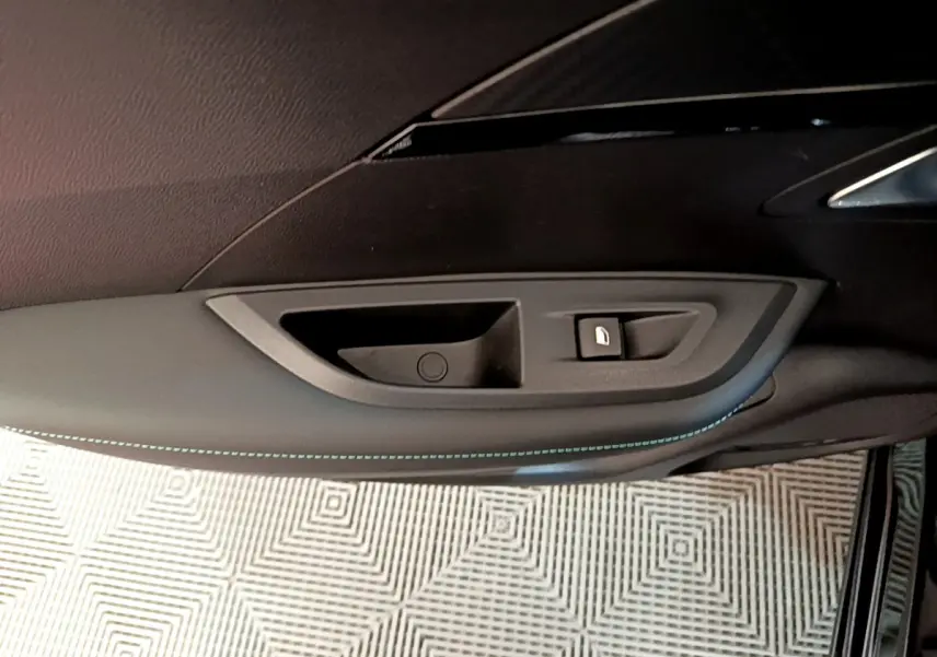 Gros plan sur la poignée intérieure côté gauche de la porte d'une Peugeot 2008 noire avec couture bleue décorative.