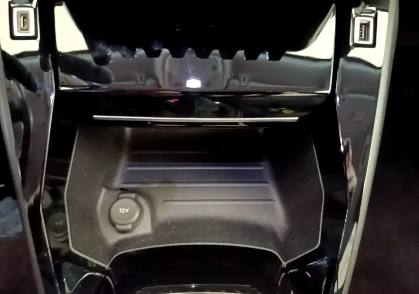 Gros plan sur la console centrale noire du Peugeot 2008, montrant la prise 12V et les finitions brillantes autour.